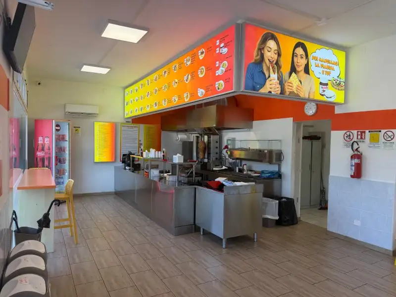 L'interno del locale con il bancone, la cucina a vista e il tabellone con i piatti del menu
